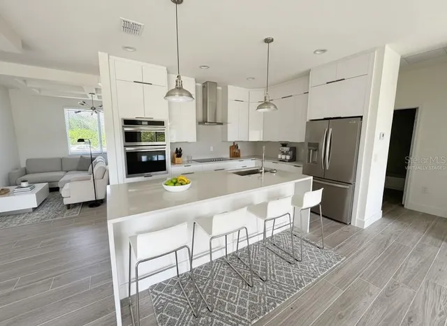 a kitchen with stainless steel appliances kitchen island granite countertop a refrigerator a stove a sink and white cabinets with wooden floor