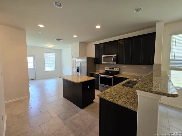 a kitchen with granite countertop wooden cabinets a counter top space and stainless steel appliances