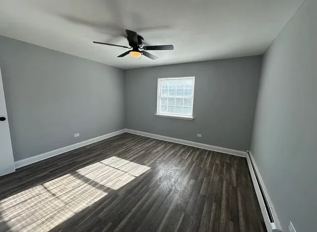 an empty room with wooden floor fan and windows