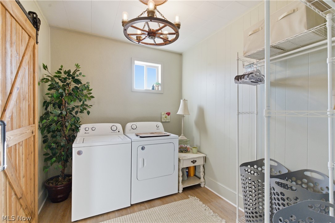 52450 Tower Road Cumberland, OH 43732 - Photo 8 of 41 Laundry room with light wood finished floors, a barn door, hanging lights, washer and clothes dryer, and wood walls