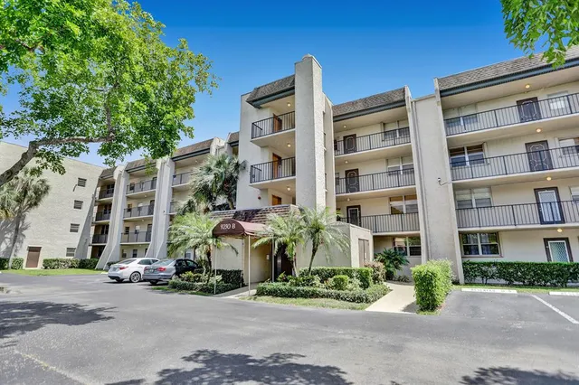 a front view of multi story residential apartment building with yard and parking