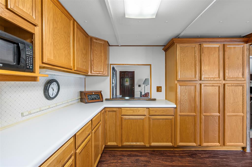 3667 Oak Circle Weatherford, TX 76088 - Photo 21 of 35 Kitchen featuring light countertops, dark wood-style flooring, backsplash, black microwave, and brown cabinets