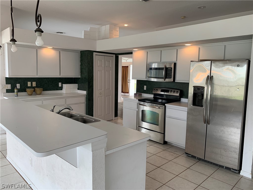 212 Danby Road Lehigh Acres, FL 33936 - Photo 6 of 21 a kitchen with a refrigerator a microwave a sink and white cabinets