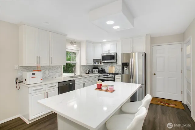 a kitchen with stainless steel appliances a stove a sink dishwasher a refrigerator white cabinets and wooden floor