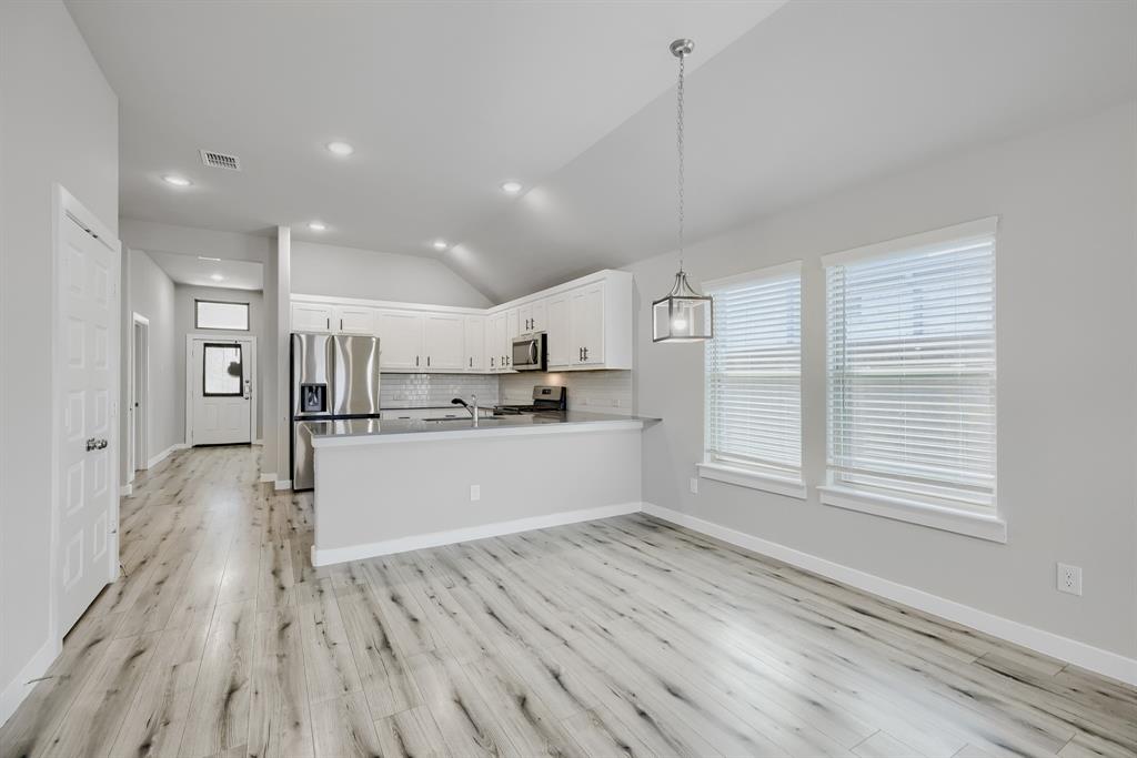 114 Mandarin Street Forney, TX 75126 - Photo 4 of 11 Open-concept living space featuring wood-finish flooring, vaulted ceilings with recessed lighting, a modern kitchen with white cabinetry and stainless steel appliances, and a dining area with a contemporary pendant light and multiple windows