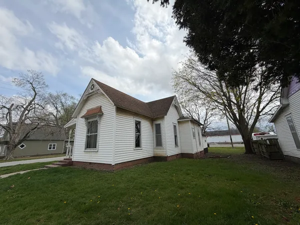a view of a white house next to a yard with big trees