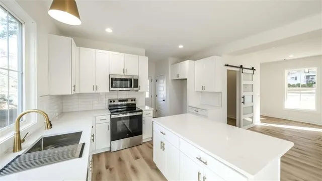 a large kitchen with stainless steel appliances granite countertop a stove a sink a refrigerator and white cabinets with wooden floor