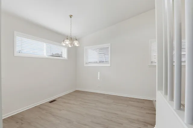 an empty room with wooden floor chandelier and windows