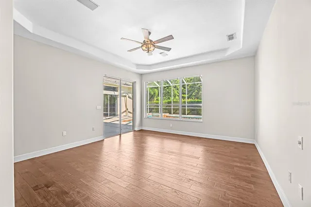 a view of an empty room with wooden floor and a ceiling fan
