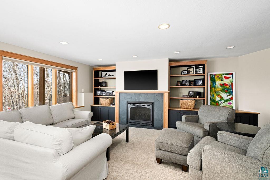 4856 Kingston Street Duluth, MN 55804 - Photo 41 of 88 Spacious living area featuring a fireplace with stone surround, custom built-in shelving, large windows with natural wood trim, recessed lighting, and neutral carpet flooring