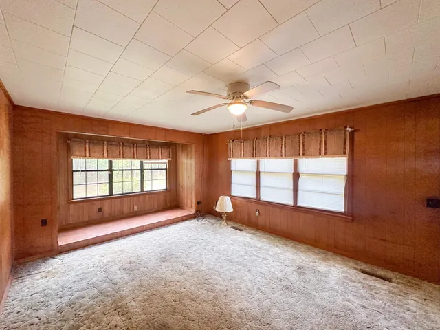 an empty room with chandelier fan and windows