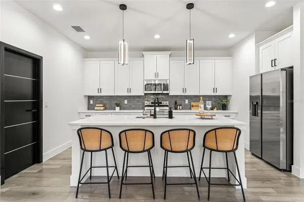 a kitchen with stainless steel appliances granite countertop a refrigerator a sink a stove a dining table and chairs with wooden floor