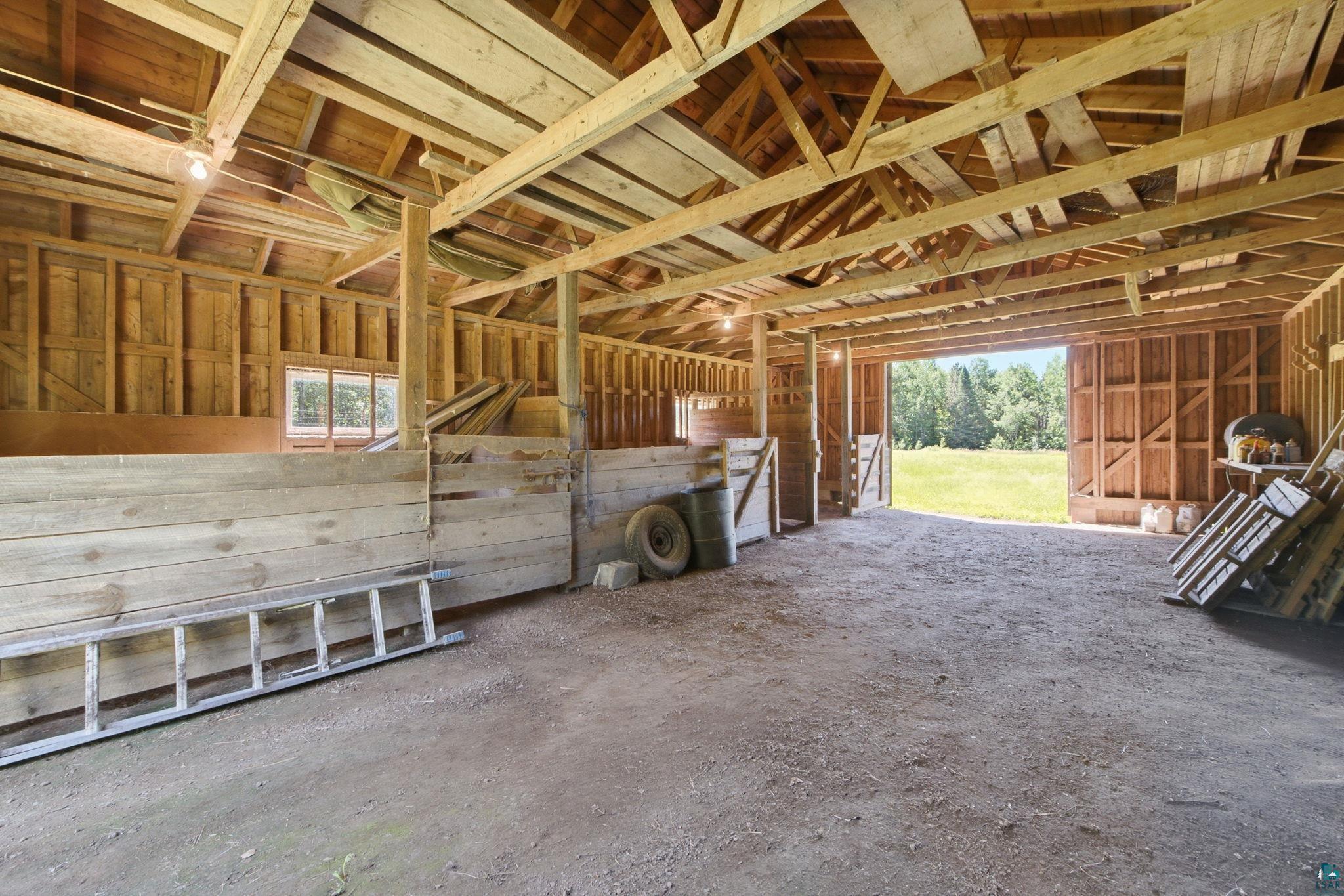 27485 South Kane Road Ashland, WI 54806 - Photo 20 of 35 Spacious barn interior featuring exposed wood beams, wood plank wall construction, and a large open doorway leading to an expansive grassy area