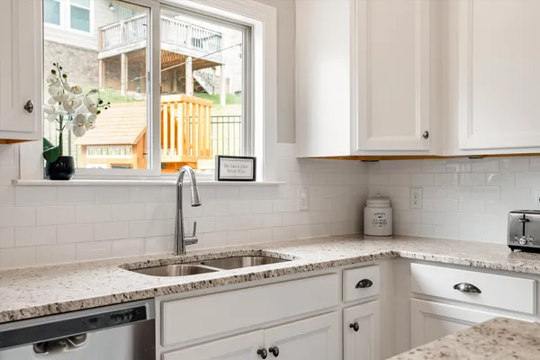 a kitchen with granite countertop a sink stainless steel appliances white cabinets and a window
