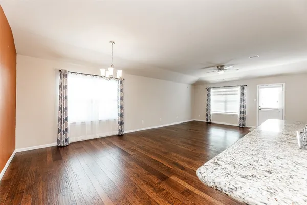 an empty room with wooden floor chandelier and windows