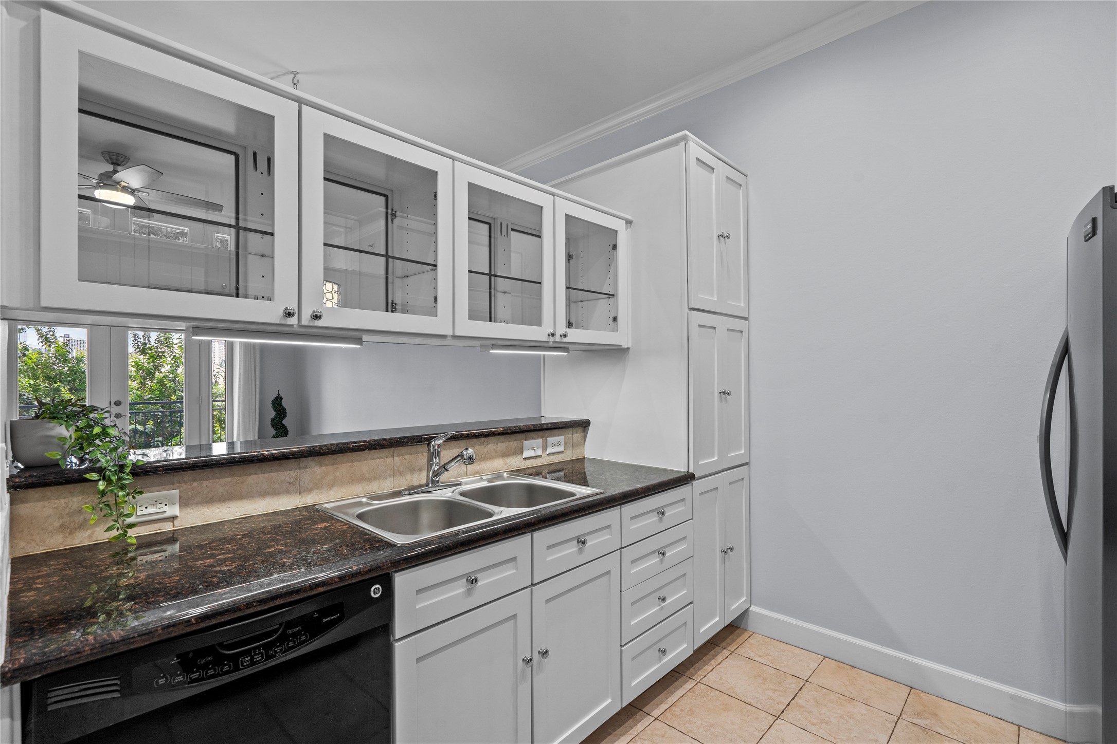1900 Genesee Street, Unit 203 Houston, TX 77006 - Photo 11 of 30 This kitchen features sleek white cabinetry with glass doors, granite countertops, and modern stainless steel appliances. It has a double sink, tile flooring, and ample natural light from a window above the counter.
