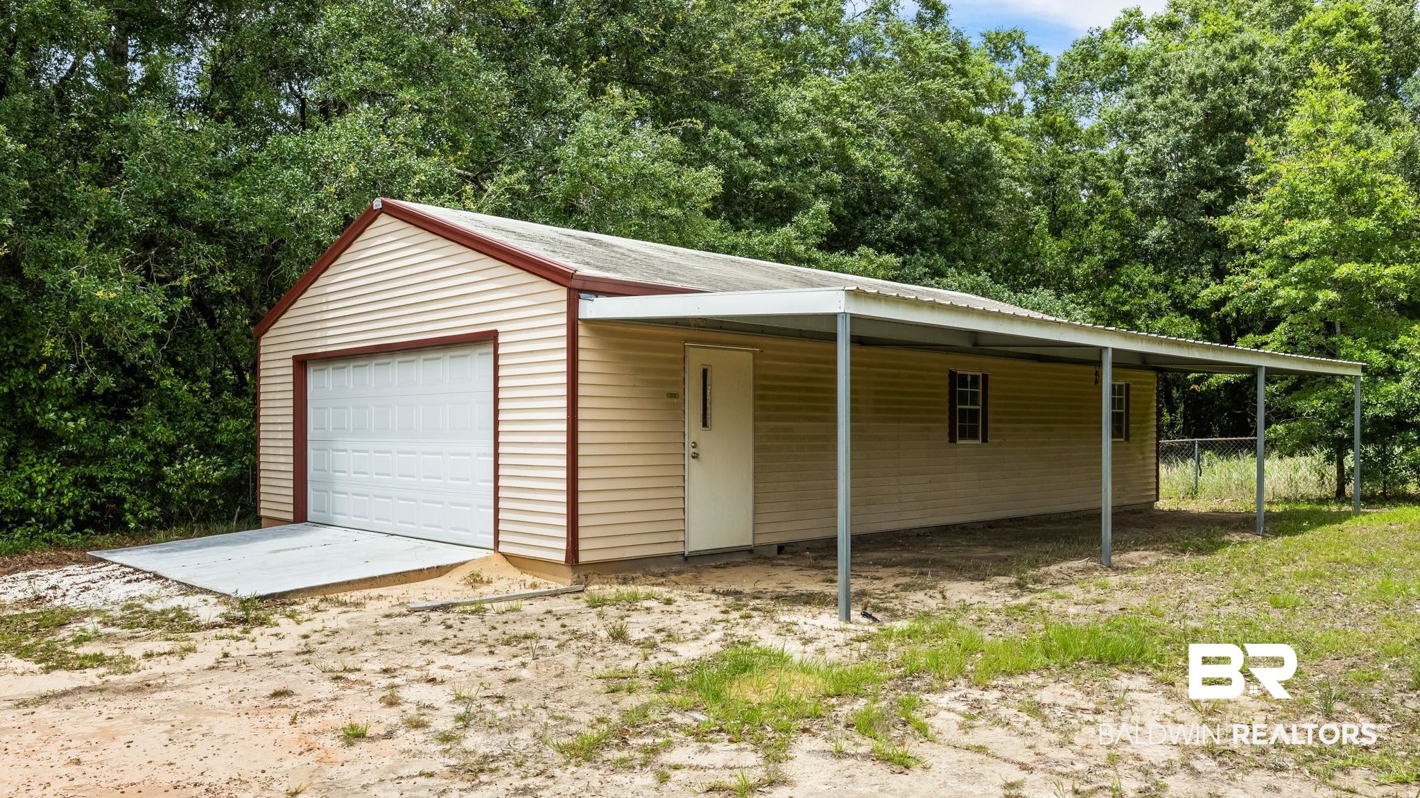 15096 Highland Circle Foley, AL 36535 - Photo 48 of 52 Detached structure featuring a large garage door with a concrete ramp, an exterior entry door, and an extended carport