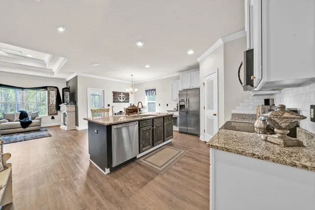 a room with kitchen island granite countertop stainless steel appliances a sink and wooden floor