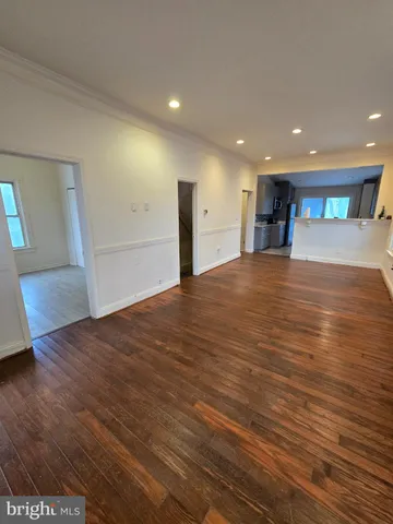 a view of an empty room with wooden floor and a kitchen