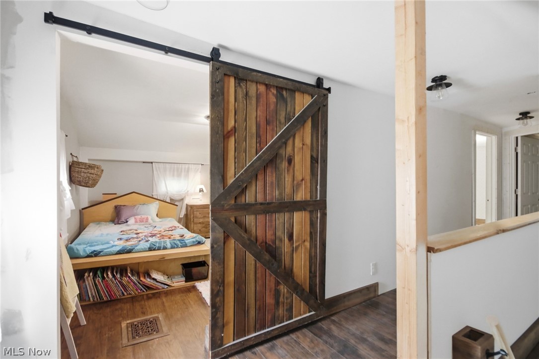 2591 Wayland Road Deerfield, OH 44411 - Photo 21 of 46 Reclaimed wood barn door on a black metal track, opening to a room featuring light wood-finish flooring and a built-in bed frame with integrated shelving