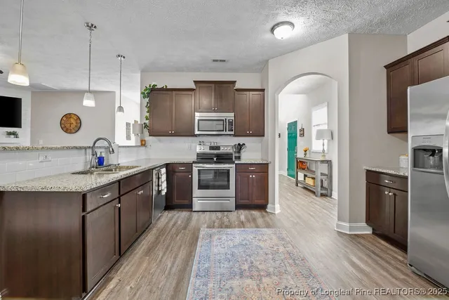 a large kitchen with stainless steel appliances granite countertop a stove a sink dishwasher a microwave oven and a refrigerator with wooden cabinets