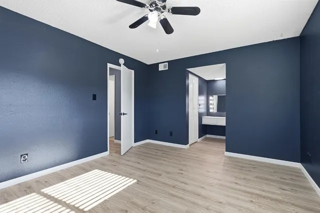 a view of an empty room with wooden floor and a ceiling fan