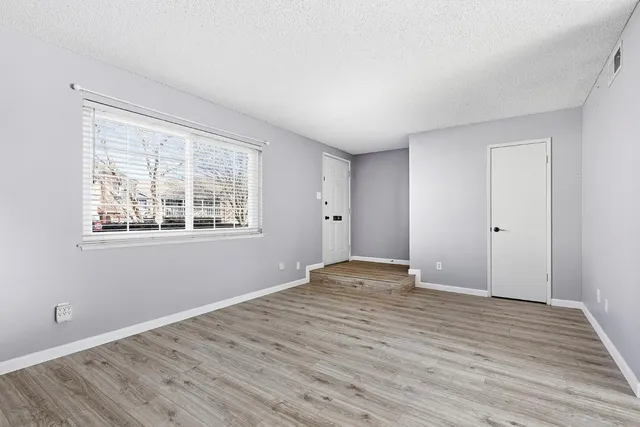 a view of an empty room with wooden floor and a window