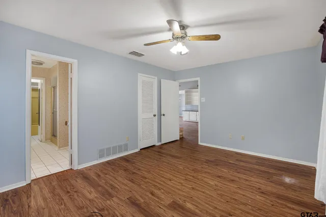 an empty room with wooden floor fan and windows