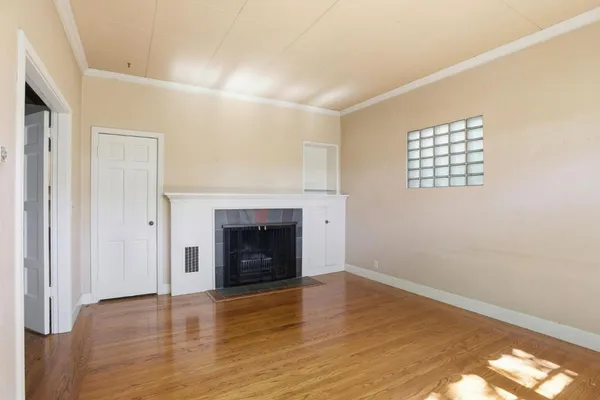 a view of an empty room with wooden floor fireplace and a window