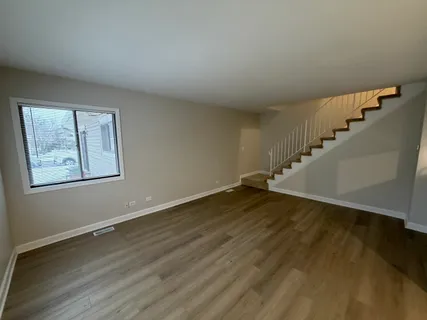a view of an empty room with wooden floor and stairs