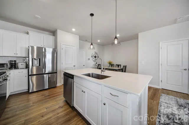 a kitchen with a sink a refrigerator a stove and white cabinets with wooden floor