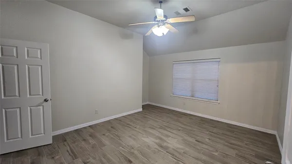 an empty room with wooden floor chandelier fan and windows
