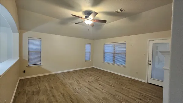 an empty room with wooden floor chandelier fan and windows