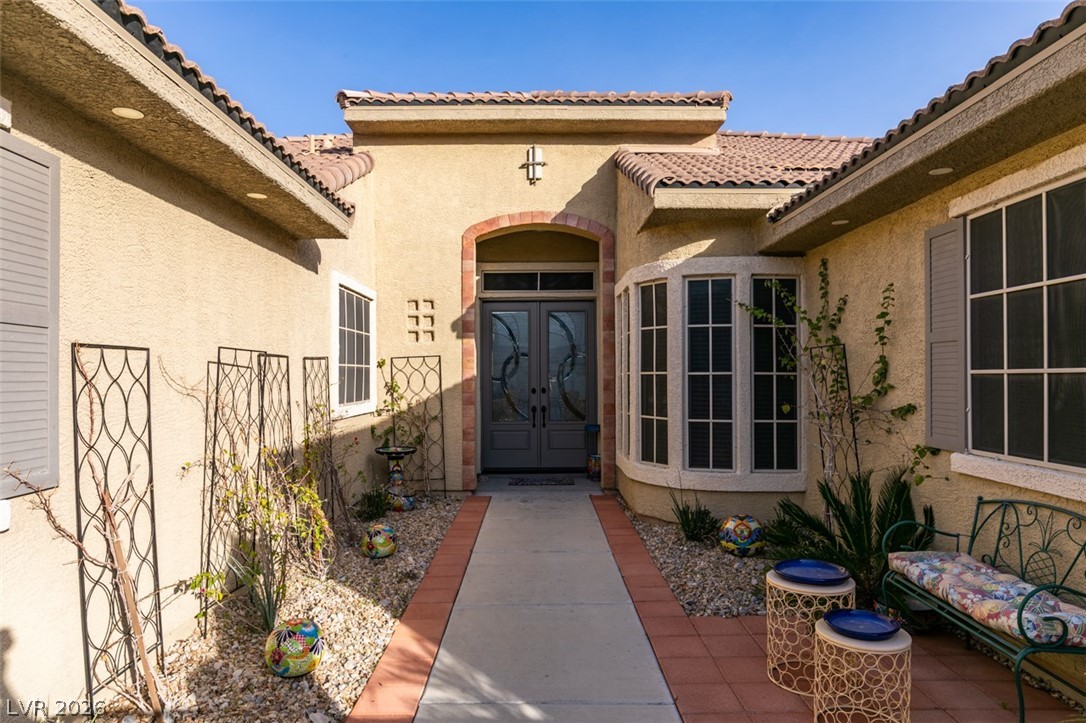 7524 Midnight Rambler Street Las Vegas, NV 89149 - Photo 4 of 51 A terracotta-tiled roof crowns this stucco-finished home, featuring an arched entry with double doors and decorative window shutters.