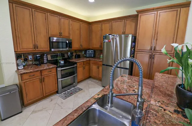 a kitchen with stainless steel appliances granite countertop a refrigerator a stove a sink dishwasher and wooden cabinets with wooden floor