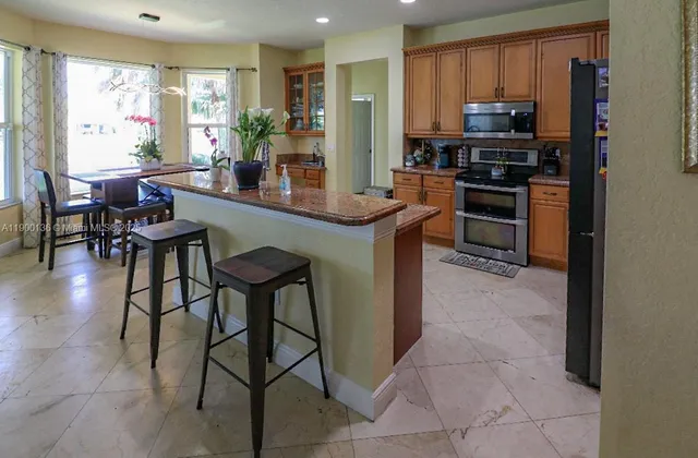 a kitchen with stainless steel appliances kitchen island granite countertop a table chairs and a refrigerator