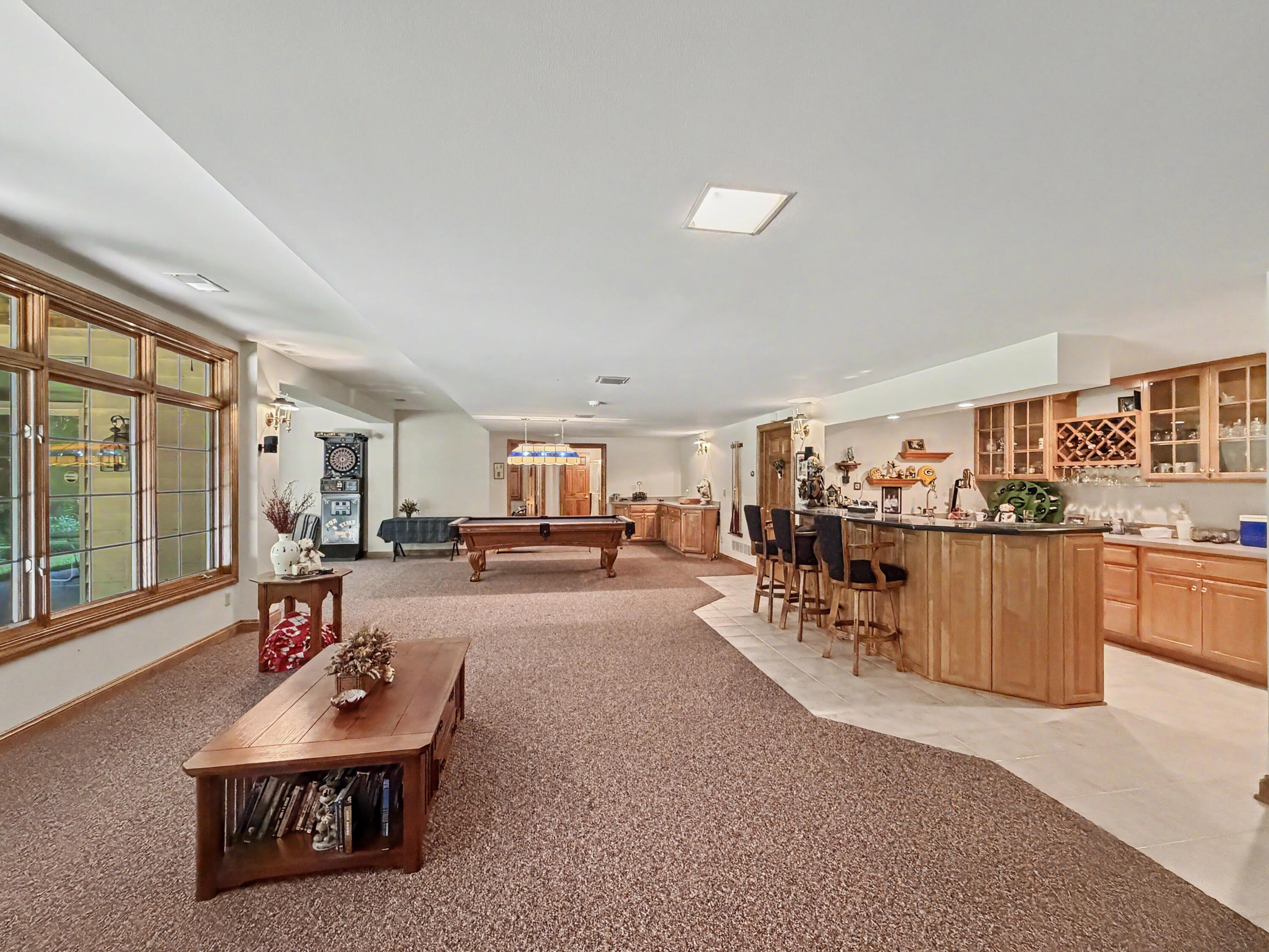 W291-s5245 Ridgefield Road Waukesha, WI 53189 - Photo 30 of 44 The fully exposed walkout lower level is designed for entertaining, featuring expansive recreation space, walls of windows, a custom wet bar with cabinetry and seating, game area, sun-filled sitting room, and direct access to the covered stamped-concrete patio. Surrounded by mature trees and a private wooded backdrop
