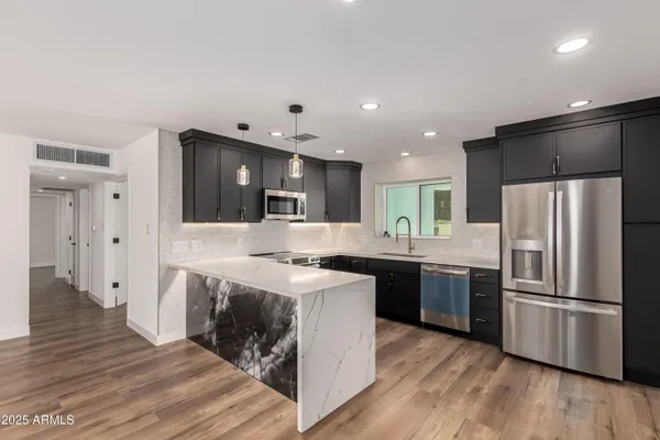 a kitchen with stainless steel appliances granite countertop a refrigerator a sink dishwasher a stove and a refrigerator with wooden floor