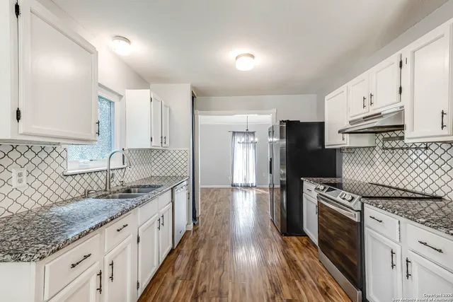 a kitchen with granite countertop a sink wooden floor and stainless steel appliances