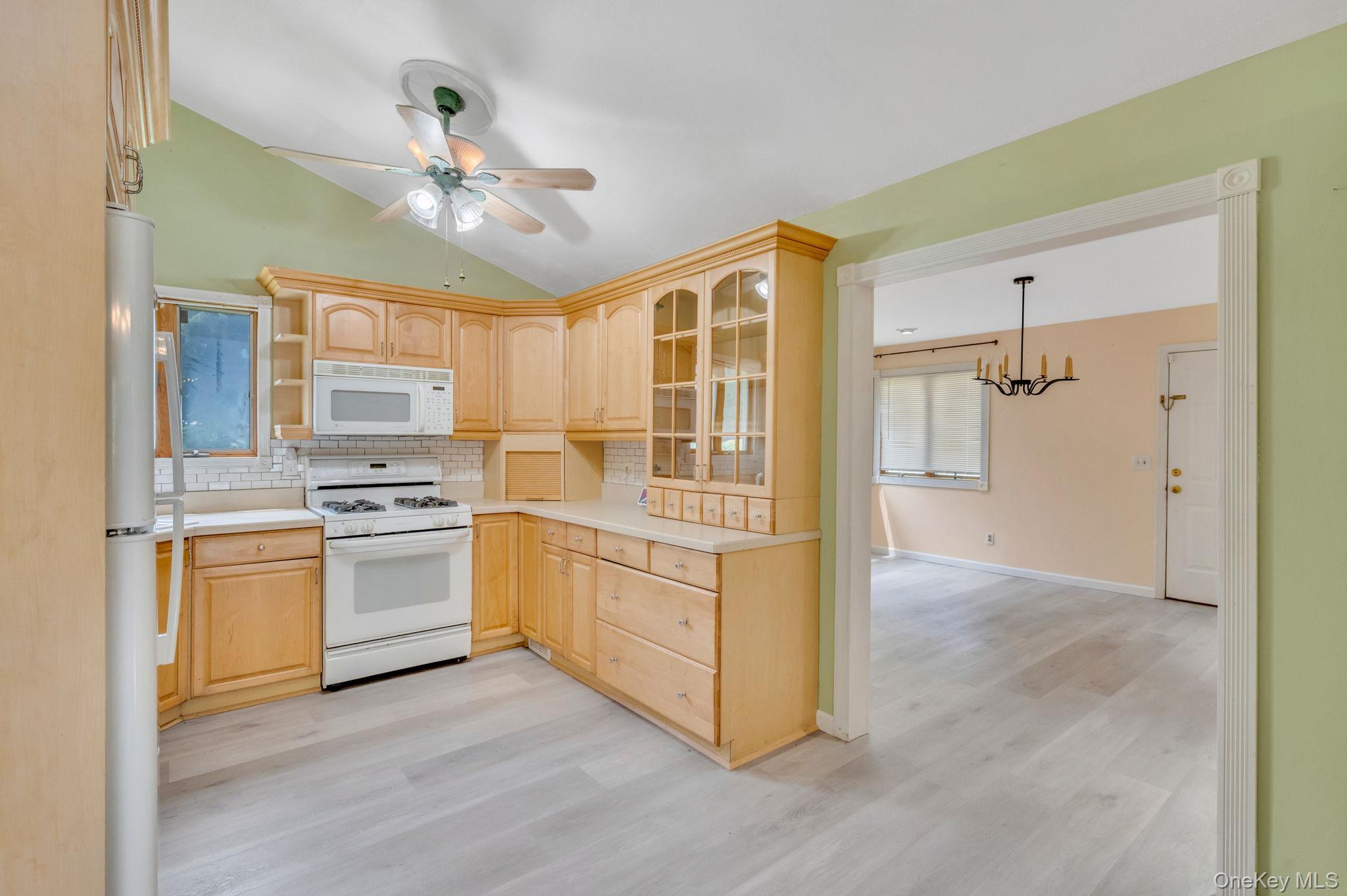 10 Laurie Road Brentwood, NY 11717 - Photo 7 of 29 Kitchen featuring light brown cabinets, white appliances, vaulted ceiling, backsplash, and light wood-type flooring