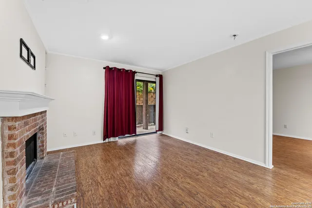 a view of an empty room with wooden floor and a fireplace