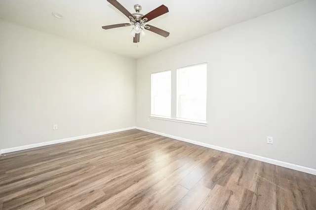 an empty room with wooden floor fan and windows
