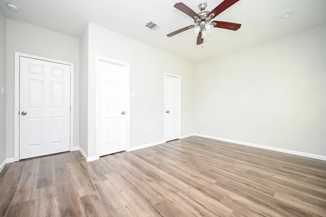 an empty room with wooden floor ceiling fan and windows