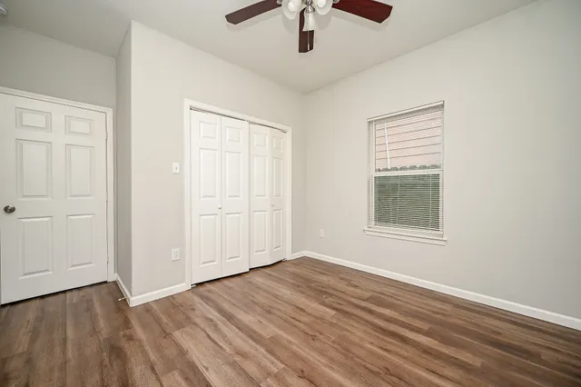an empty room with wooden floor chandelier fan and windows