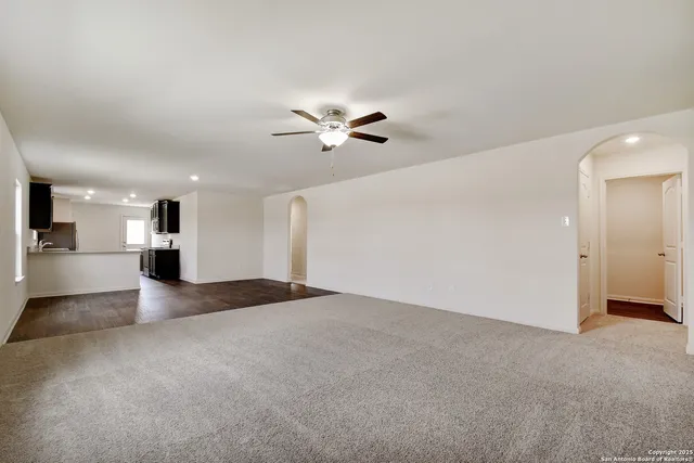a view of an empty room with a ceiling fan and kitchen view