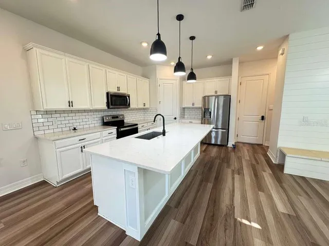 a kitchen with stainless steel appliances a refrigerator a stove top oven a sink dishwasher and white cabinets with wooden floor