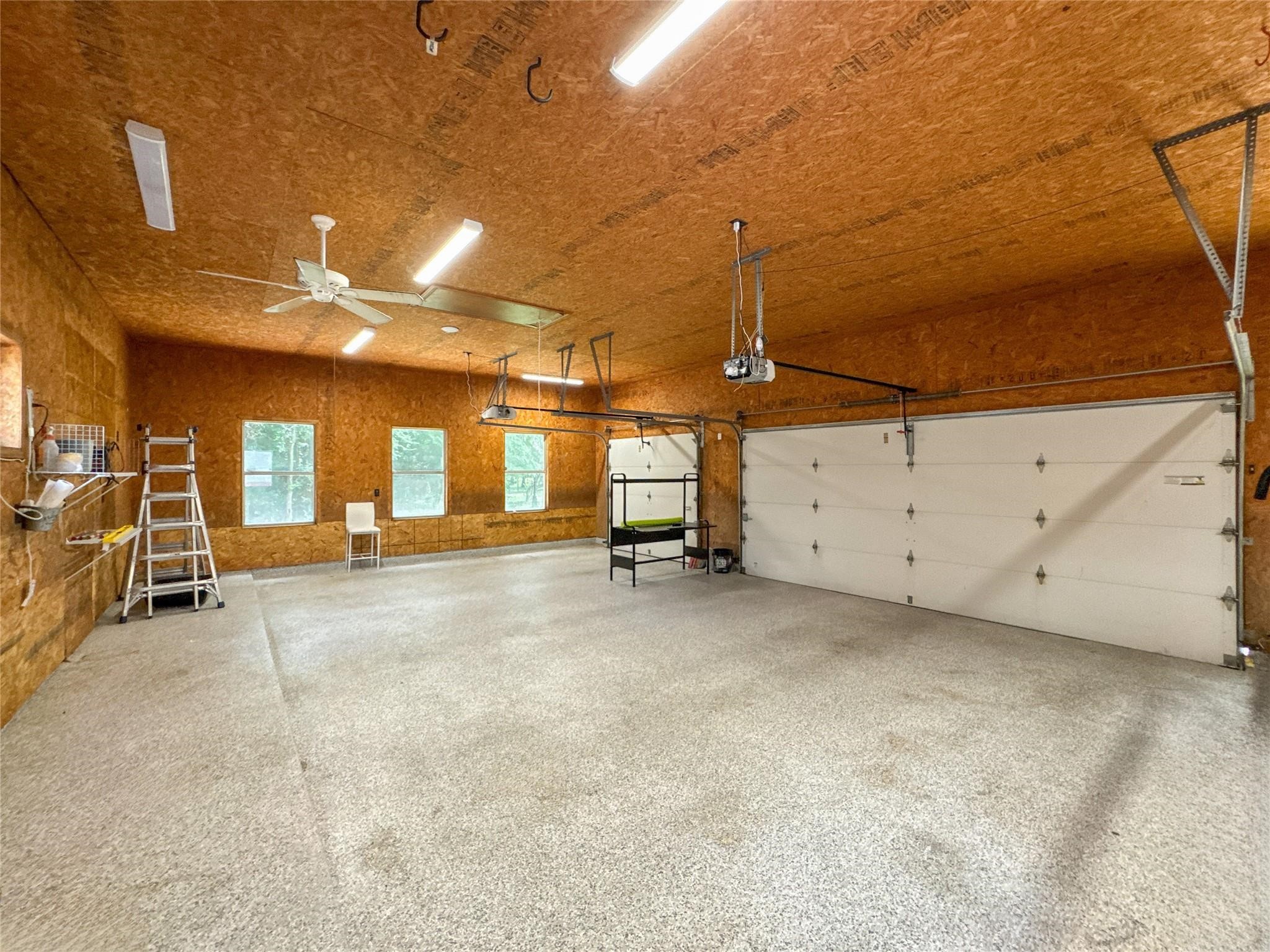 1810 Woerner Road Houston, TX 77090 - Photo 39 of 39 Spacious garage with a high ceiling, textured flooring, and ample lighting. It features two large garage doors, windows for natural light, and storage racks, making it ideal for multiple vehicles or a workshop.