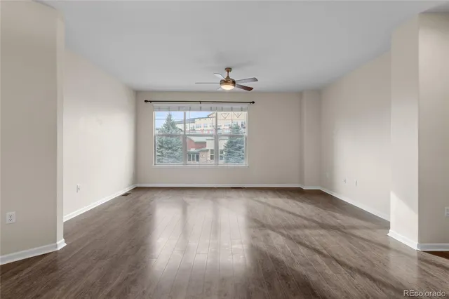 an empty room with wooden floor chandelier fan and windows
