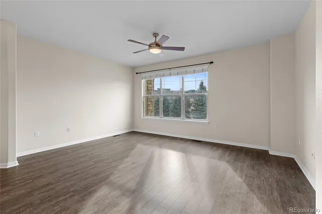 an empty room with wooden floor chandelier fan and windows