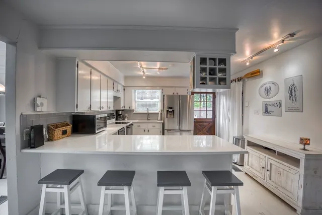 a kitchen with granite countertop a refrigerator a sink a stove and white cabinets